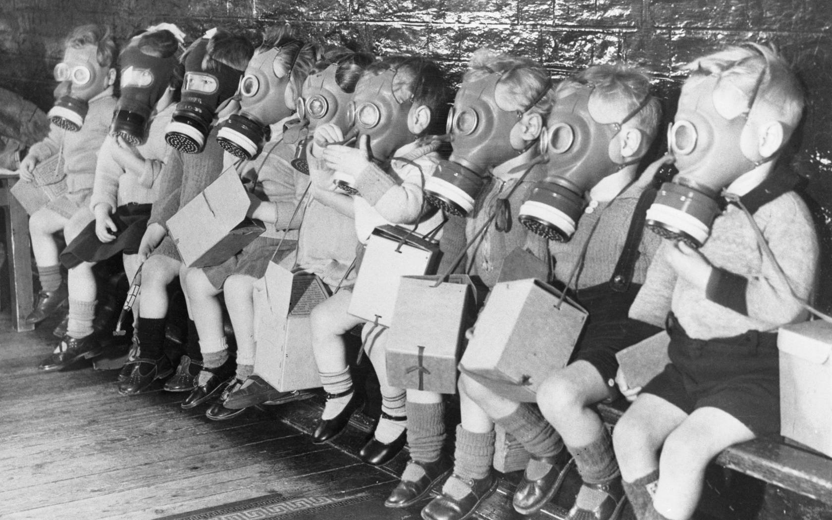 Row of children sit down with gas masks on. A warning from history.