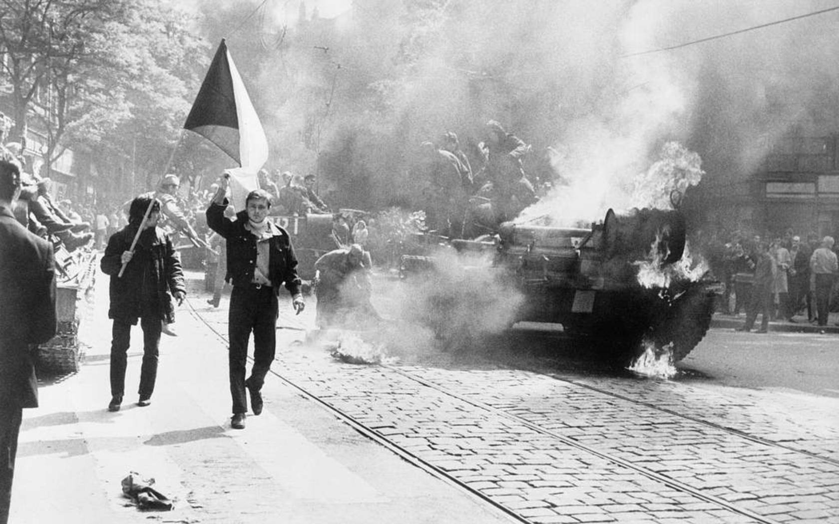 Czechoslovaks carry their national flag past a burning Soviet tank in Prague, 1968. The JIC failed to foresee Soviet retaliations to the mass protests